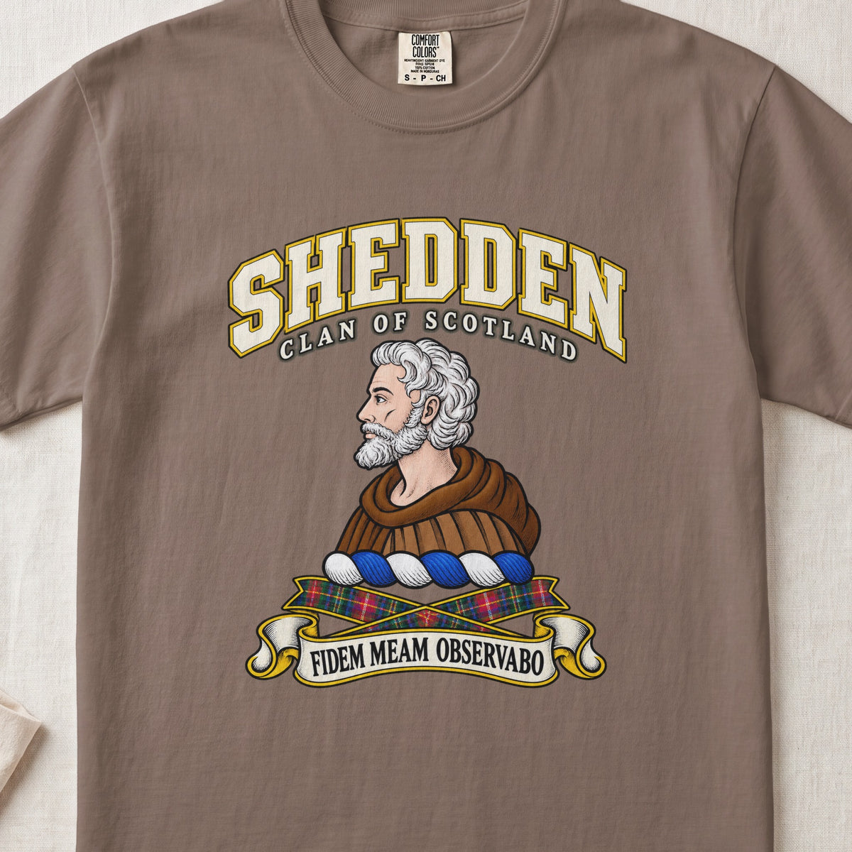 Shedden Scottish clan T-shirt in Espresso, front view with a gray-haired, bearded figure in a brown robe and motto design.