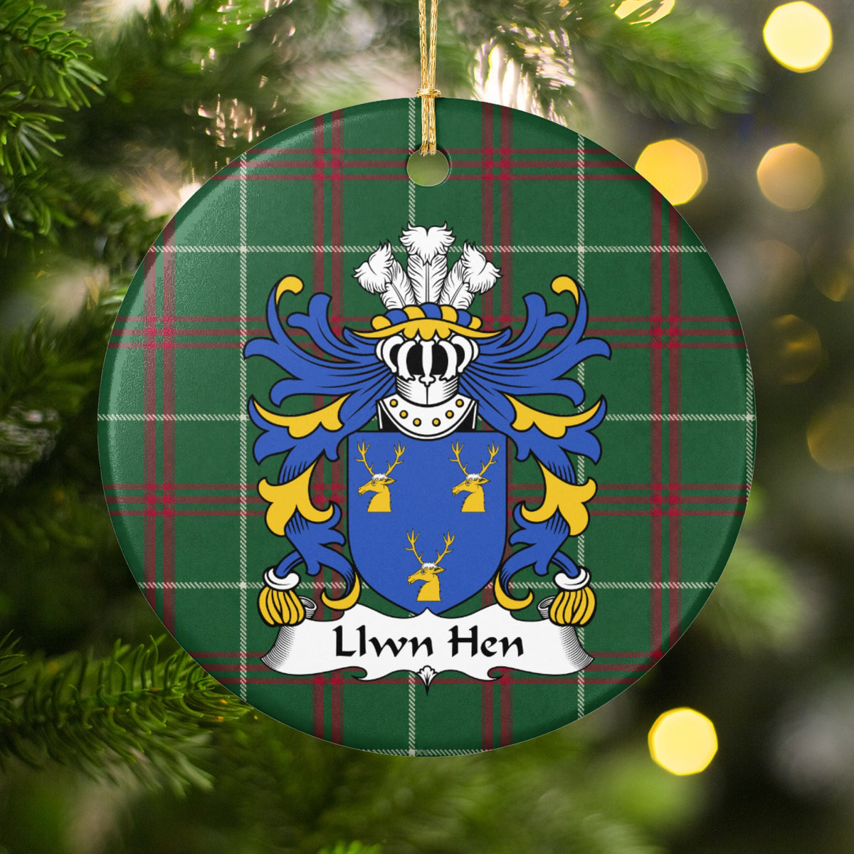 Llwn Hen ornament hanging on a Christmas tree among green branches and warm lights, with a blue shield with three gold stag heads on Welsh national tartan.