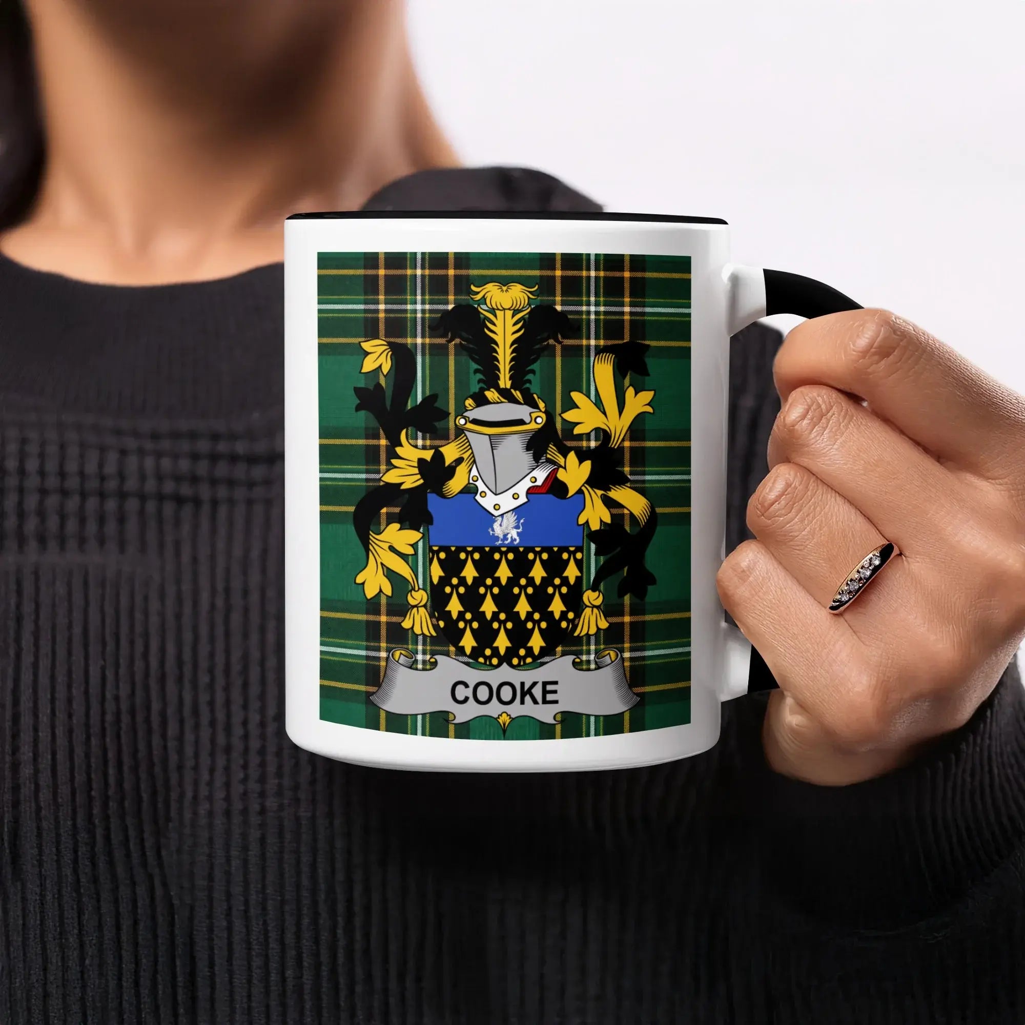 White mug with black rim and handle, featuring the Cooke family crest on a green tartan background.