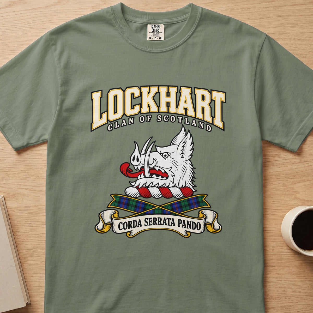 Lockhart white boar’s head and tartan ribbons graphic on a sage green Comfort Colors T-shirt, front view