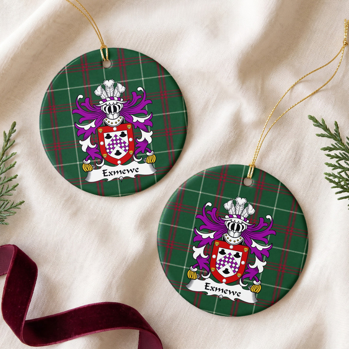 Two Exmewe ornaments on cream fabric beside burgundy ribbon; a purple-and-white checked chevron between three black shells, within a red border decorated with white circles and gold animal faces on Welsh national tartan.