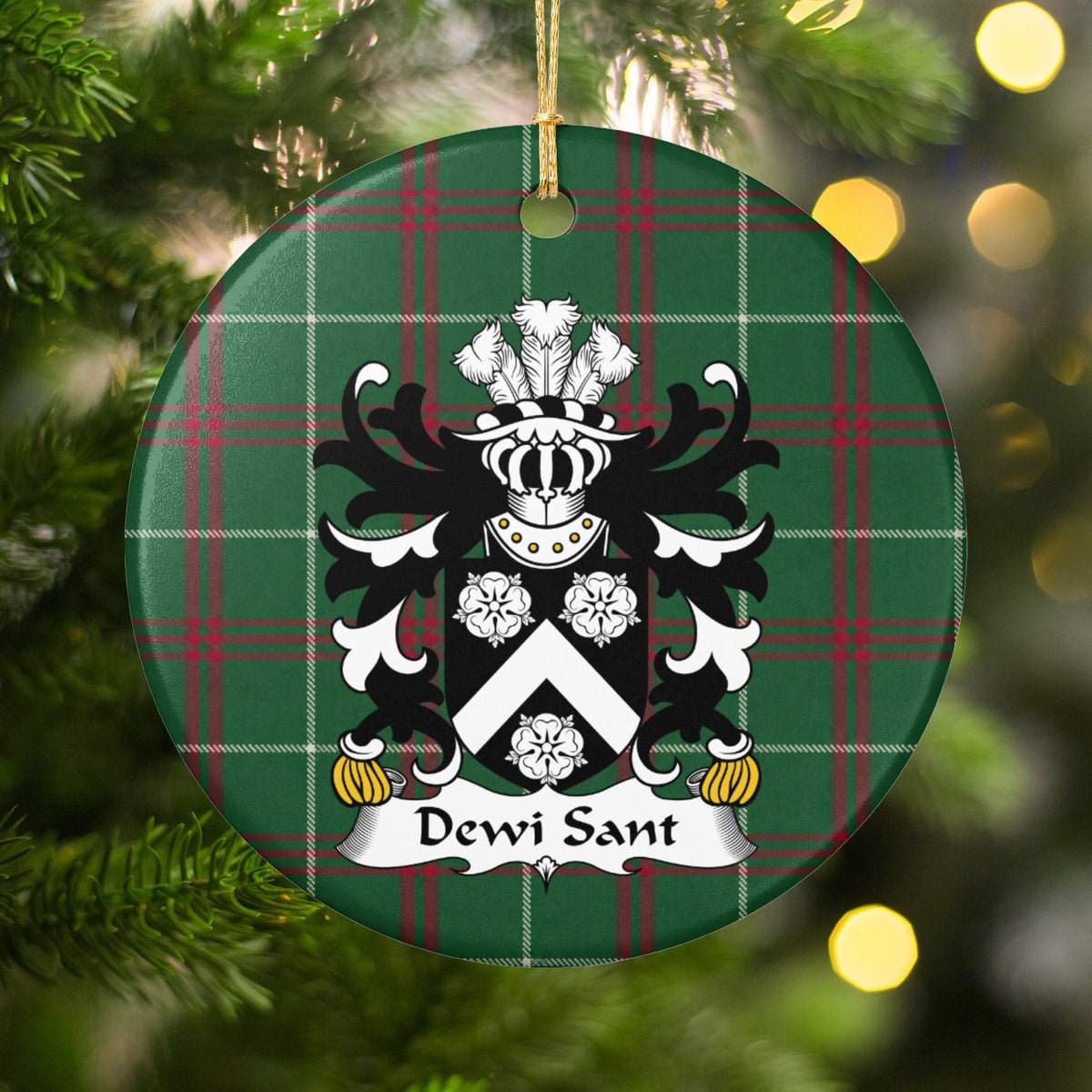 Dewi Sant ornament hanging among Christmas tree branches and warm lights; a white chevron and three white roses on a black shield on Welsh national tartan.