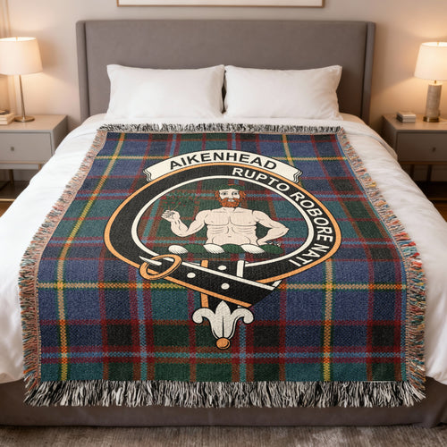 Aikenhead woven blanket displayed on a bed, with a bearded figure holding a branch on a green, blue and red tartan background