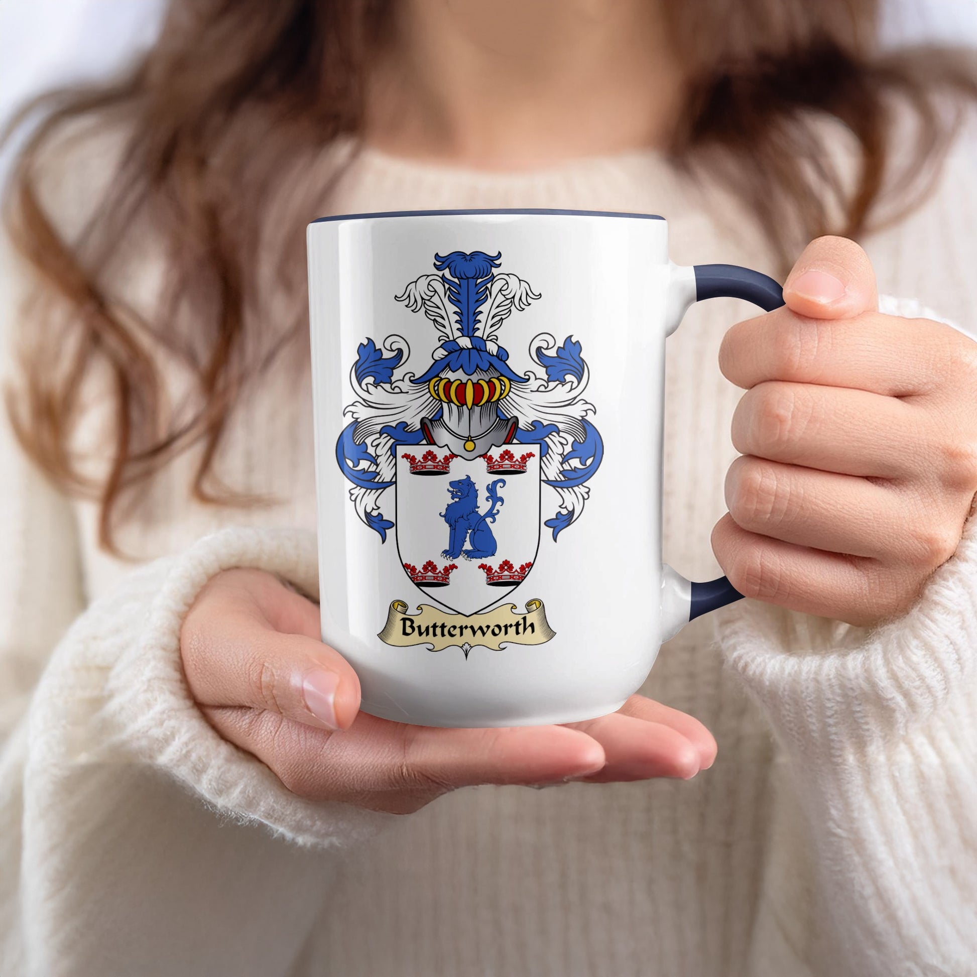 White mug with the Butterworth coat of arms and a dark blue rim, held by a person.