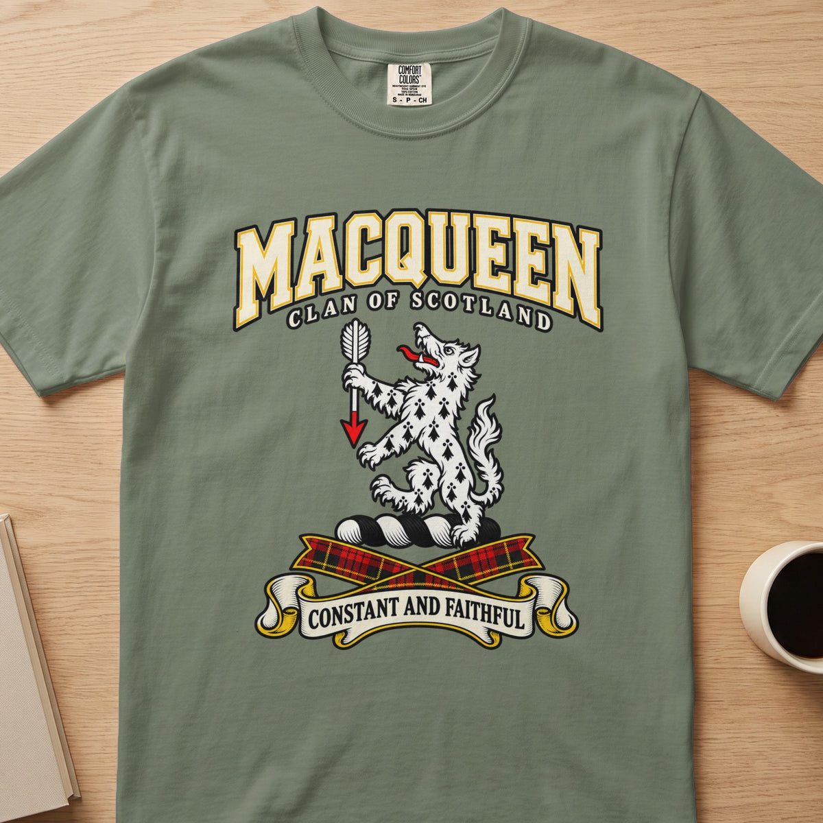 MacQueen white spotted animal crest graphic on a sage green Comfort Colors T-shirt, front view