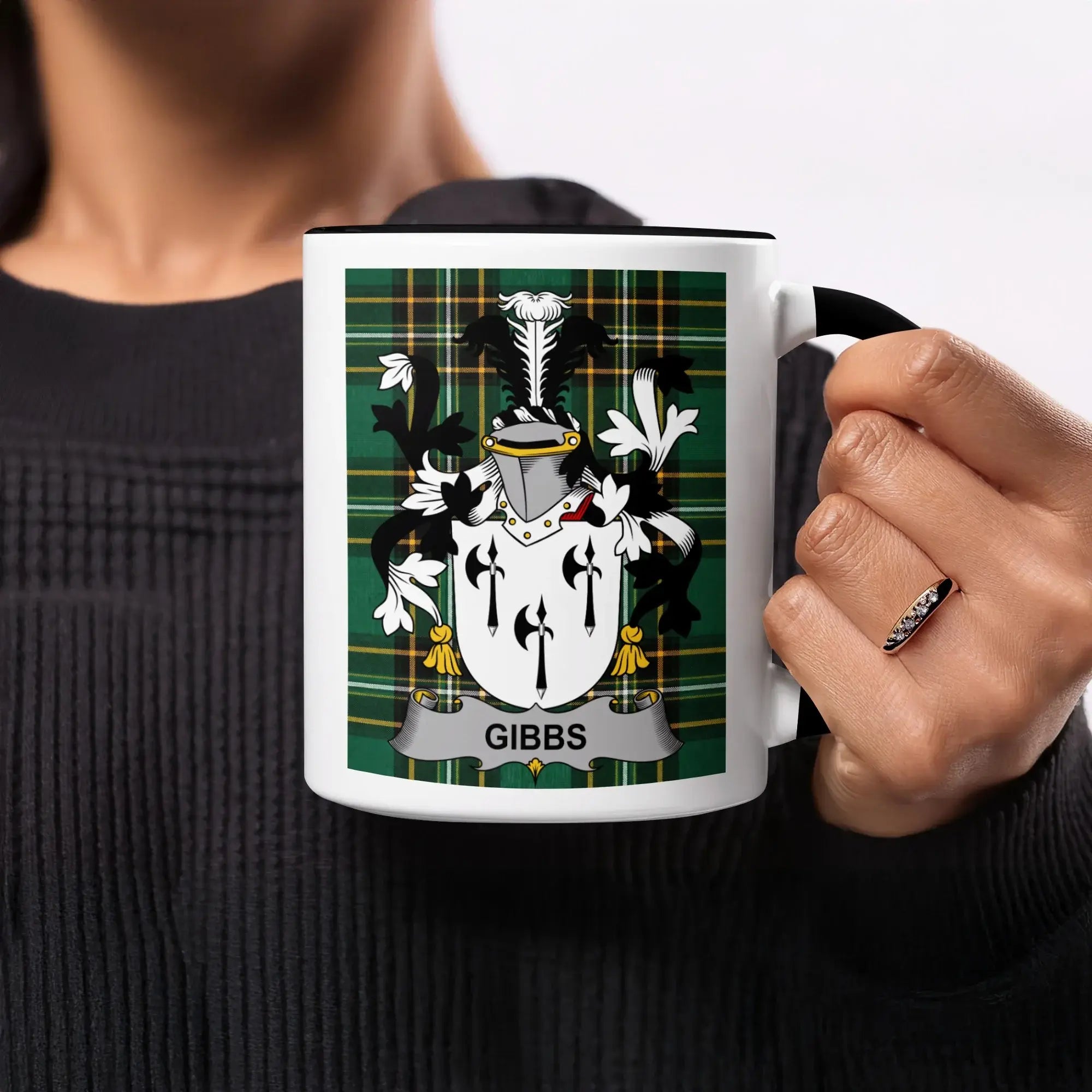 Black mug with Gibbs family crest on a green plaid background.