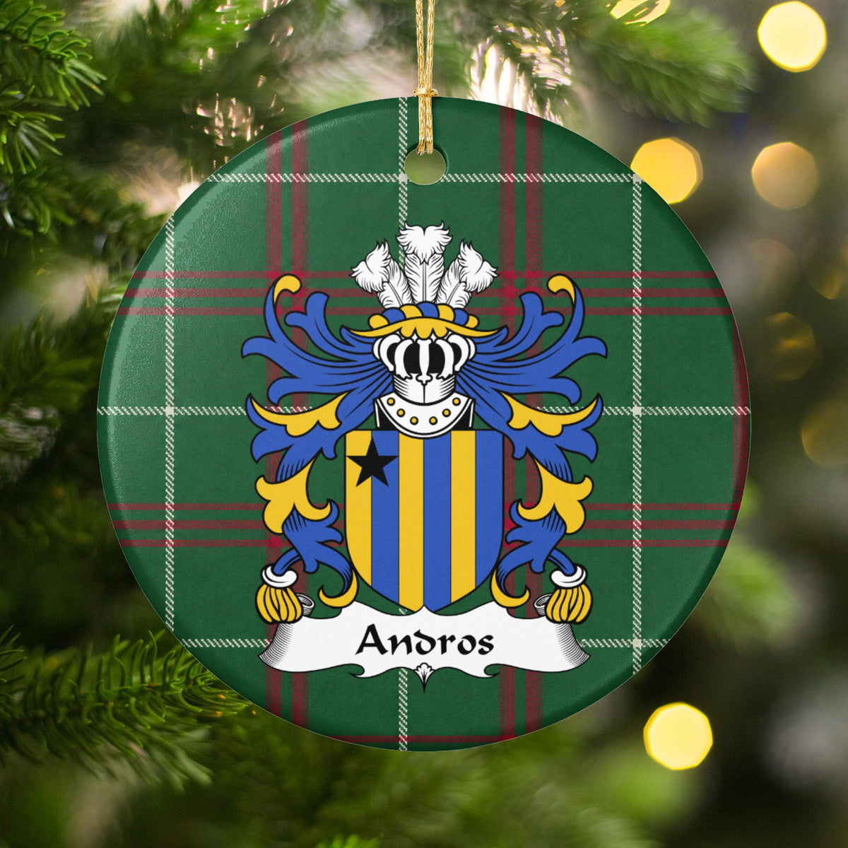 Andros family crest and surname on a round Welsh national tartan ornament, hanging by a gold cord among Christmas tree branches and warm golden lights.