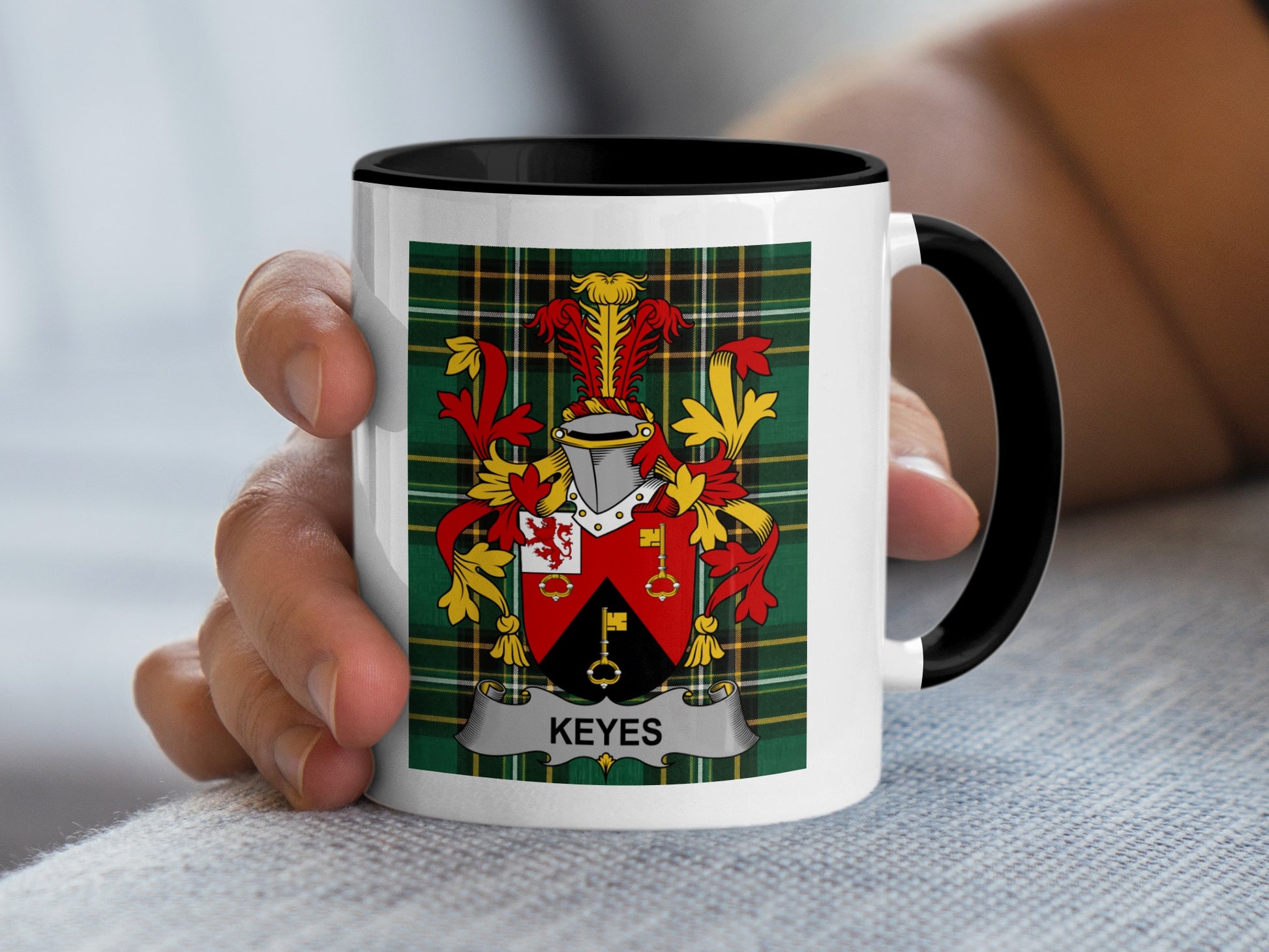White mug with black rim displaying the Keyes family crest on a green tartan background.