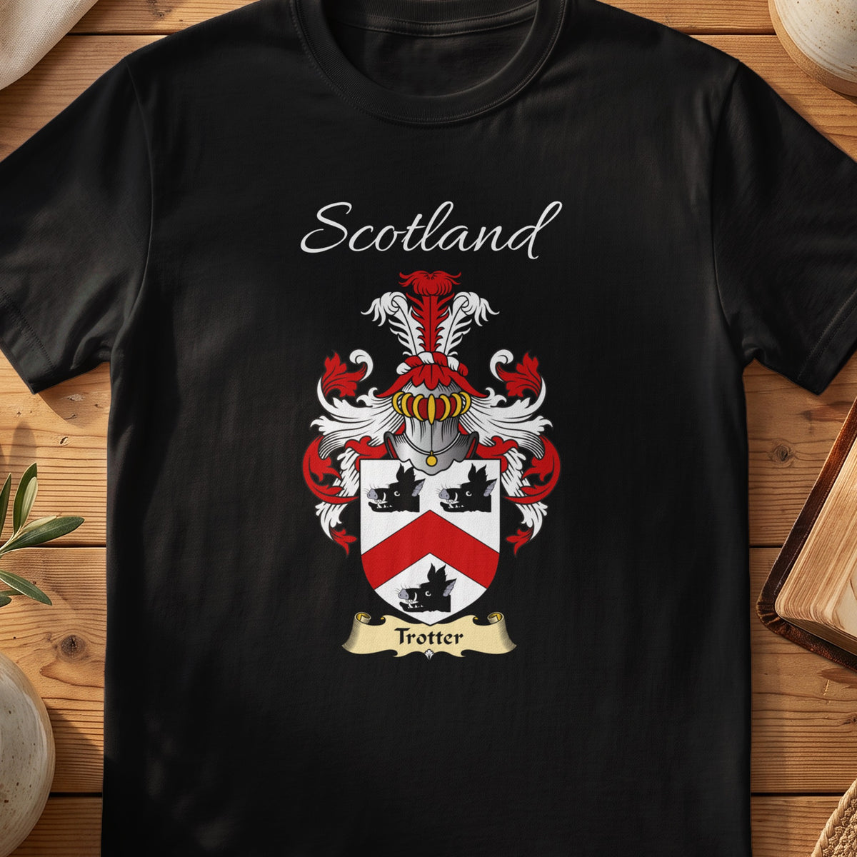Black Trotter Scottish family crest T-shirt laid flat, showing “Scotland” above a red-and-silver shield with a dark chevron and small animal-like figure.
