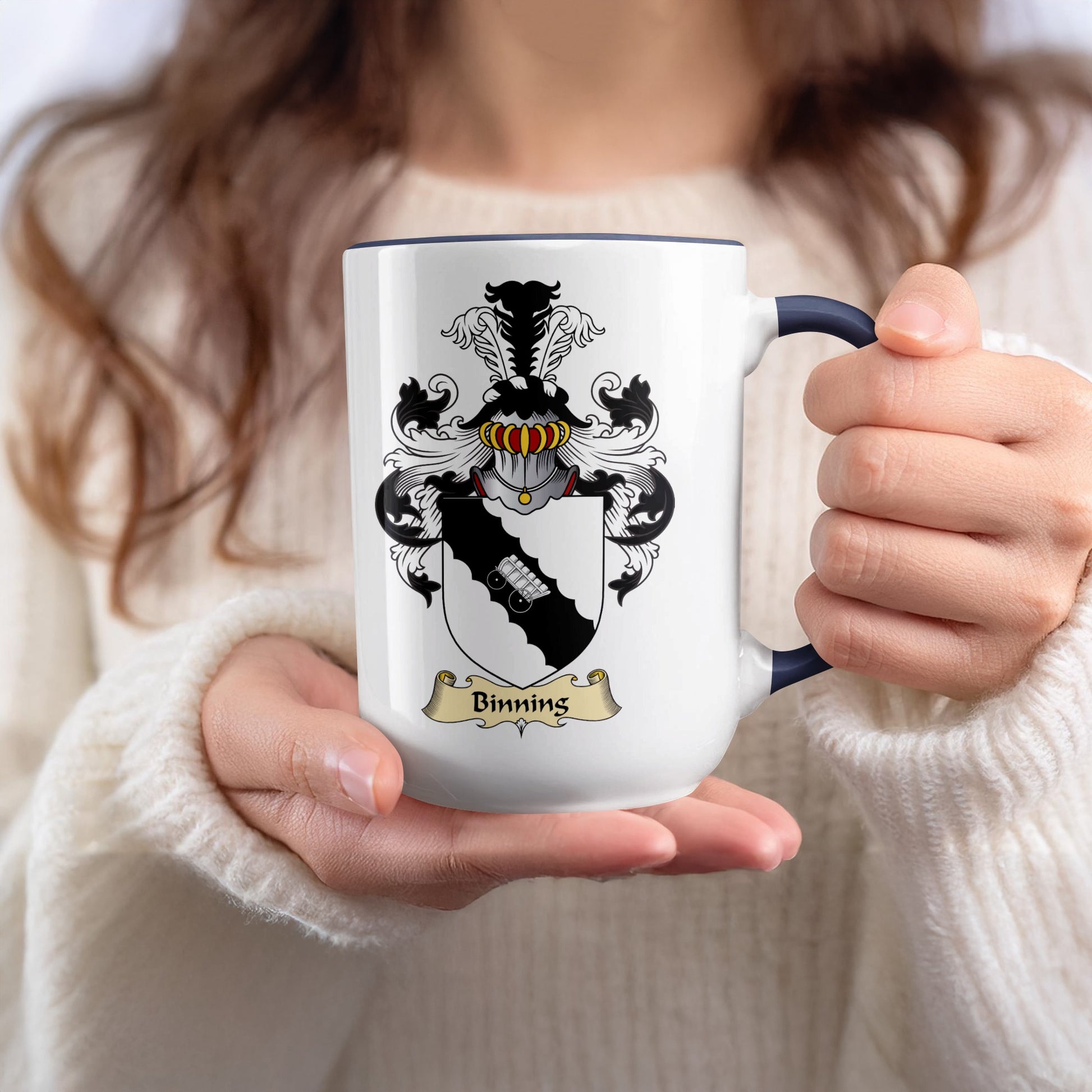 White mug with a coat of arms and "Binning" text, held by hands.