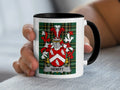 Mug with Hewitt family crest on plaid background, held by hand.
