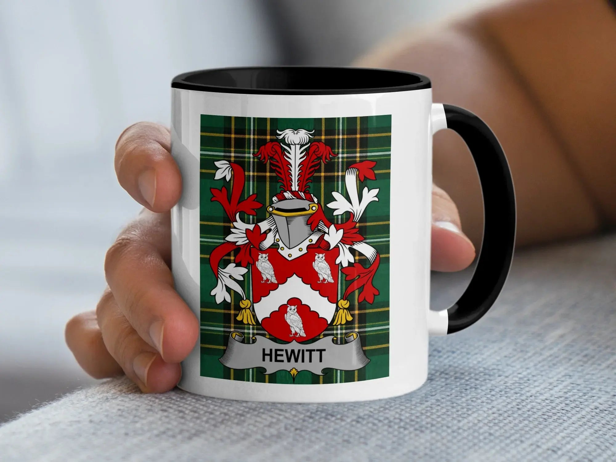 Mug with Hewitt family crest on plaid background, held by hand.