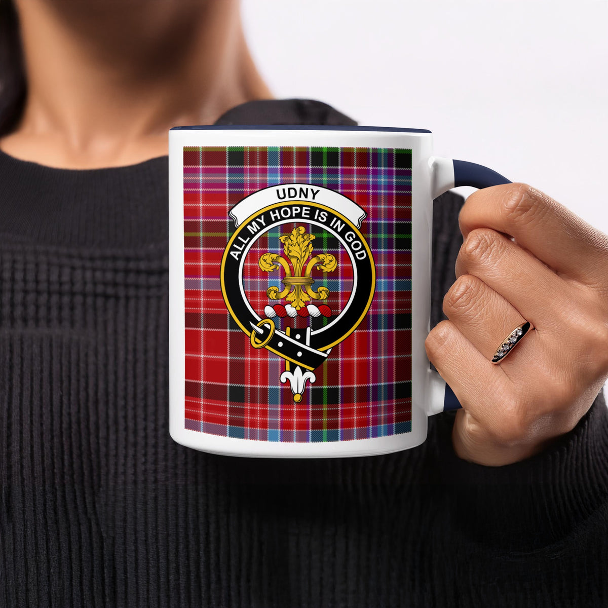Close-up lifestyle view of Udny Scottish family crest artwork on a navy 11 oz accent mug with a tartan background