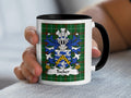 White mug with black handle featuring the Tucker family crest on a tartan background.