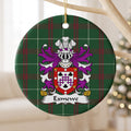 Exmewe ornament hanging from a pale wooden branch; a purple-and-white checked chevron between three black shells, within a red border decorated with white circles and gold animal faces on Welsh national tartan.