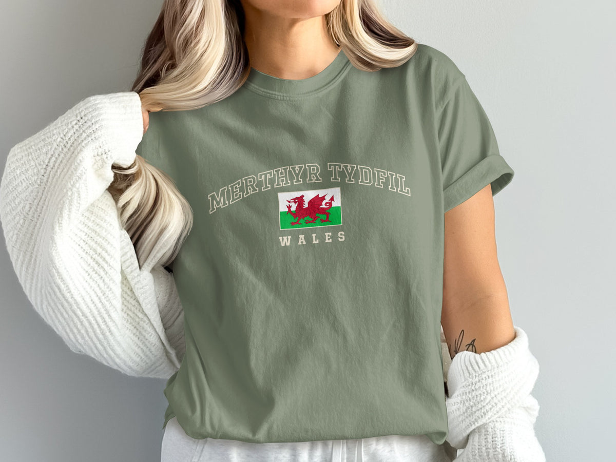 Model wearing a moss green Merthyr Tydfil Wales T-shirt with a Welsh dragon flag and a white cardigan draped off the shoulders.