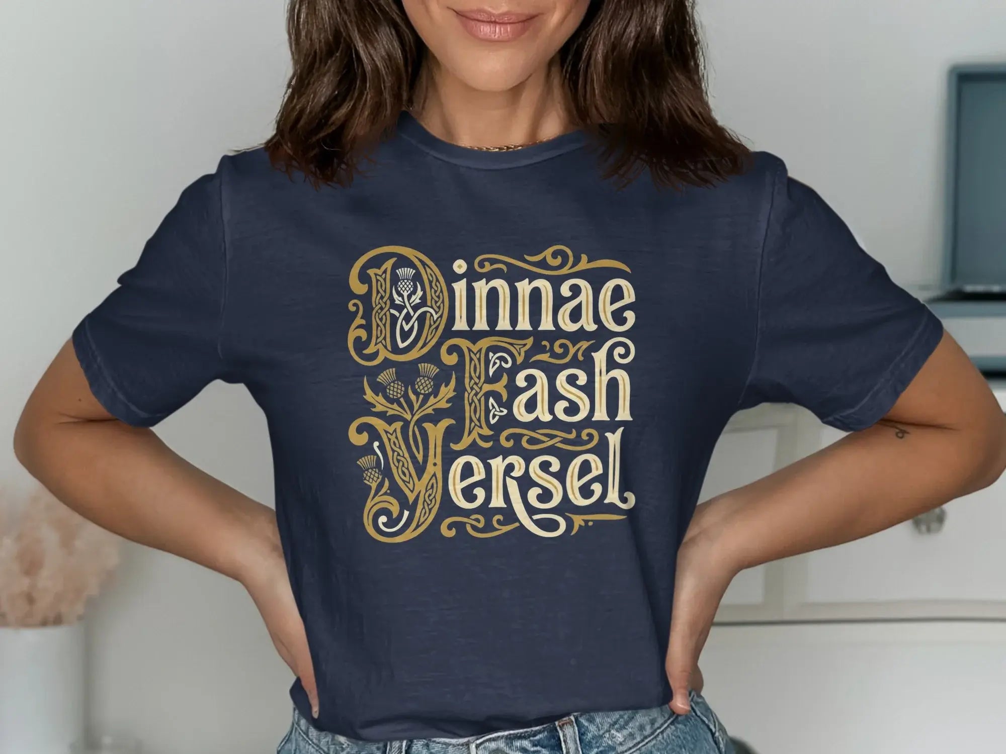 Navy t-shirt with "Dinnae Fash Yersel" in ornate gold lettering and thistle accents.