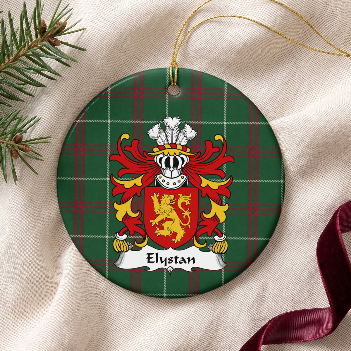 Elystan ornament on cream fabric beside evergreen and burgundy ribbon; a gold lion on a red shield on Welsh national tartan.