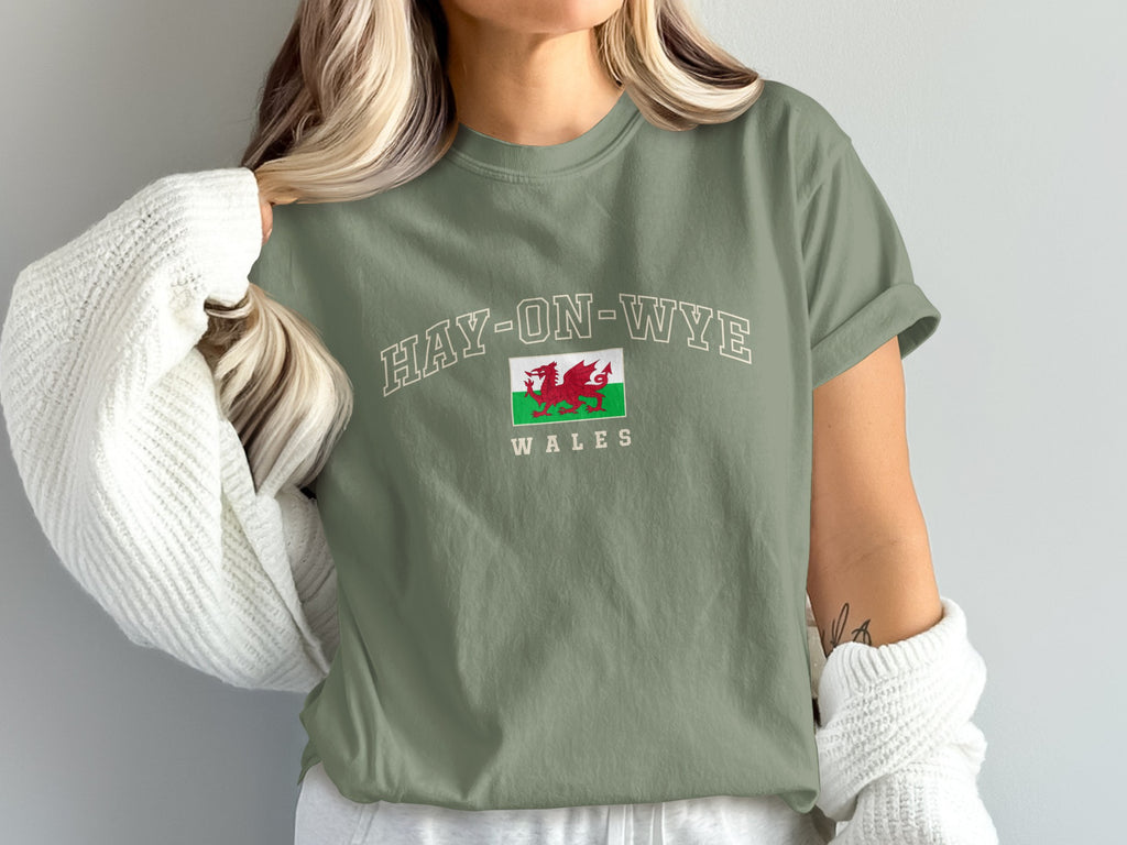 Model wearing a moss green Hay-on-Wye Wales T-shirt with a Welsh dragon flag and a white cardigan draped off the shoulders.