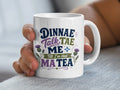 White mug with "Dinnae Talk Tae Me Till I've Had Ma Tea" text and thistles.