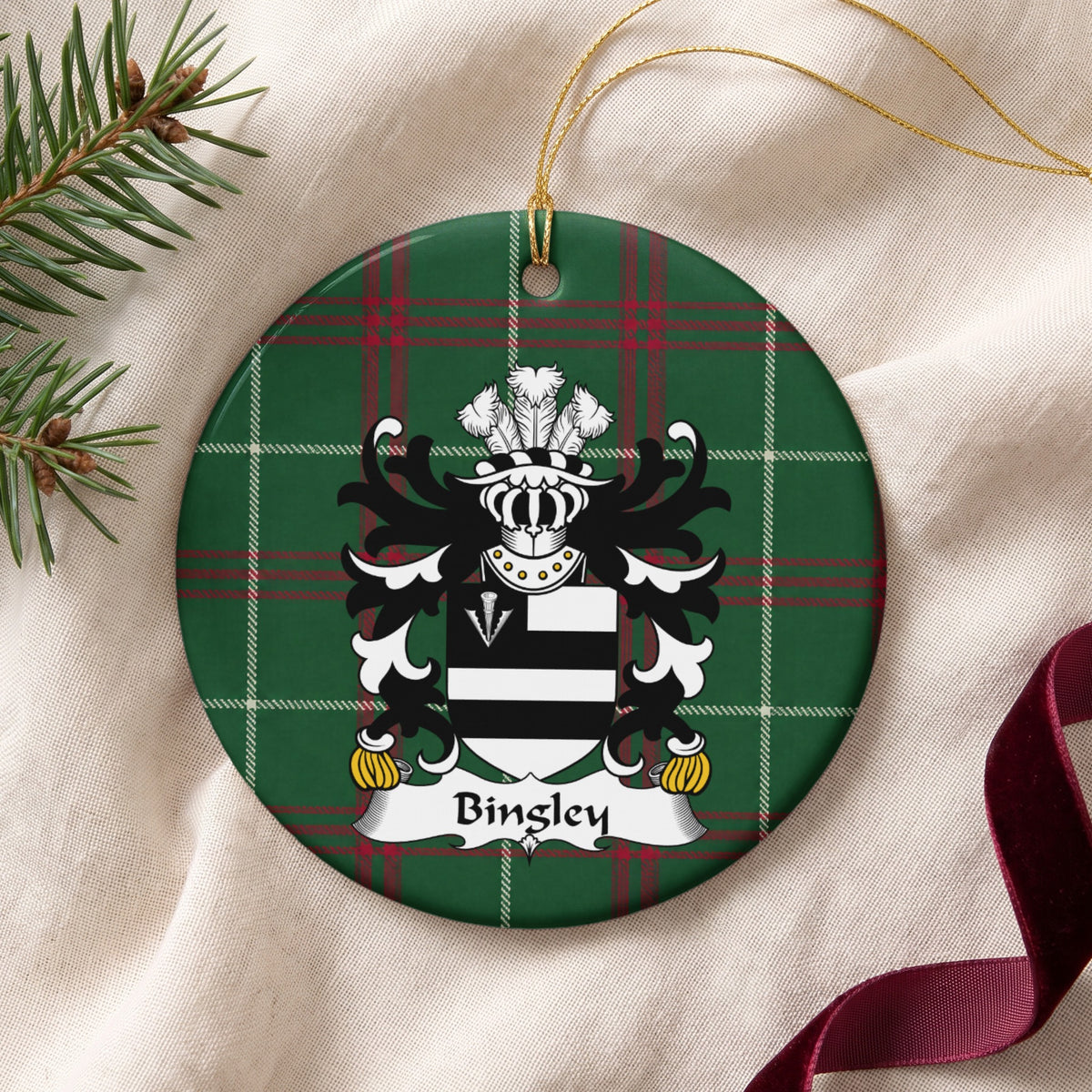 Bingley ornament on cream fabric with gold string, evergreen and burgundy ribbon; two black bars on white with a white arrowhead in a black corner panel on Welsh national tartan.