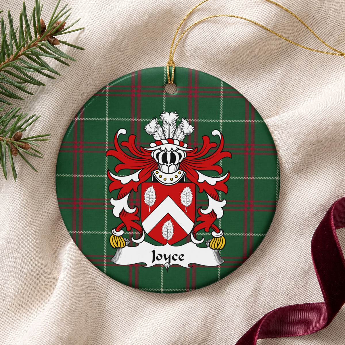 Joyce ornament on cream fabric with gold string, evergreen and burgundy ribbon; a white chevron and three white leaves on a red shield on Welsh national tartan.