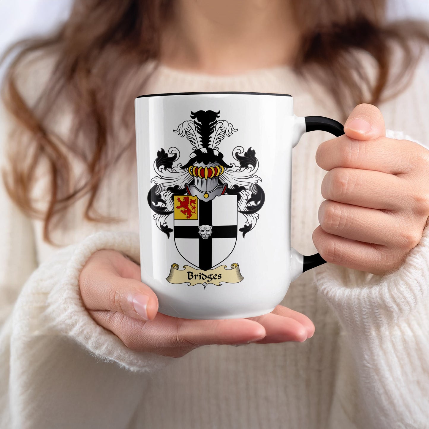 White mug with black rim displaying Bridges family crest held by hands.