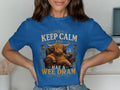 Blue t-shirt with highland cow sitting in chair, holding whisky, text reads "Keep Calm and Hae a Wee Dram".