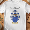 White Clunes Scottish family shield T-shirt featuring gold sprigs and white arrow-like motifs on blue