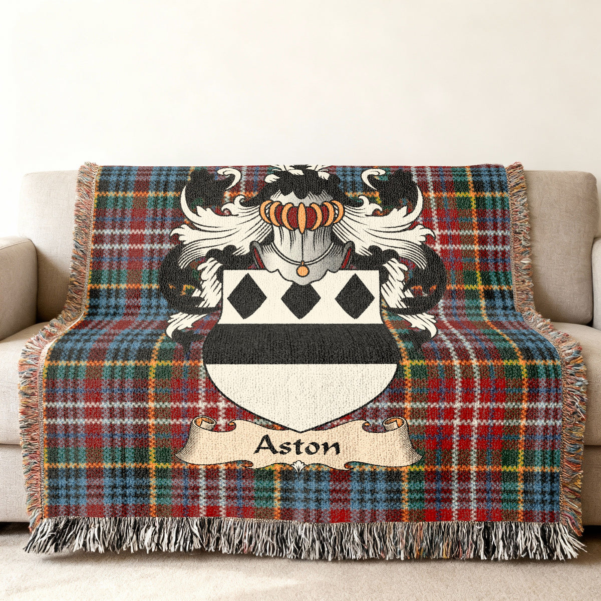 Aston Scottish family shield woven blanket with Caledonia tartan background on a sofa