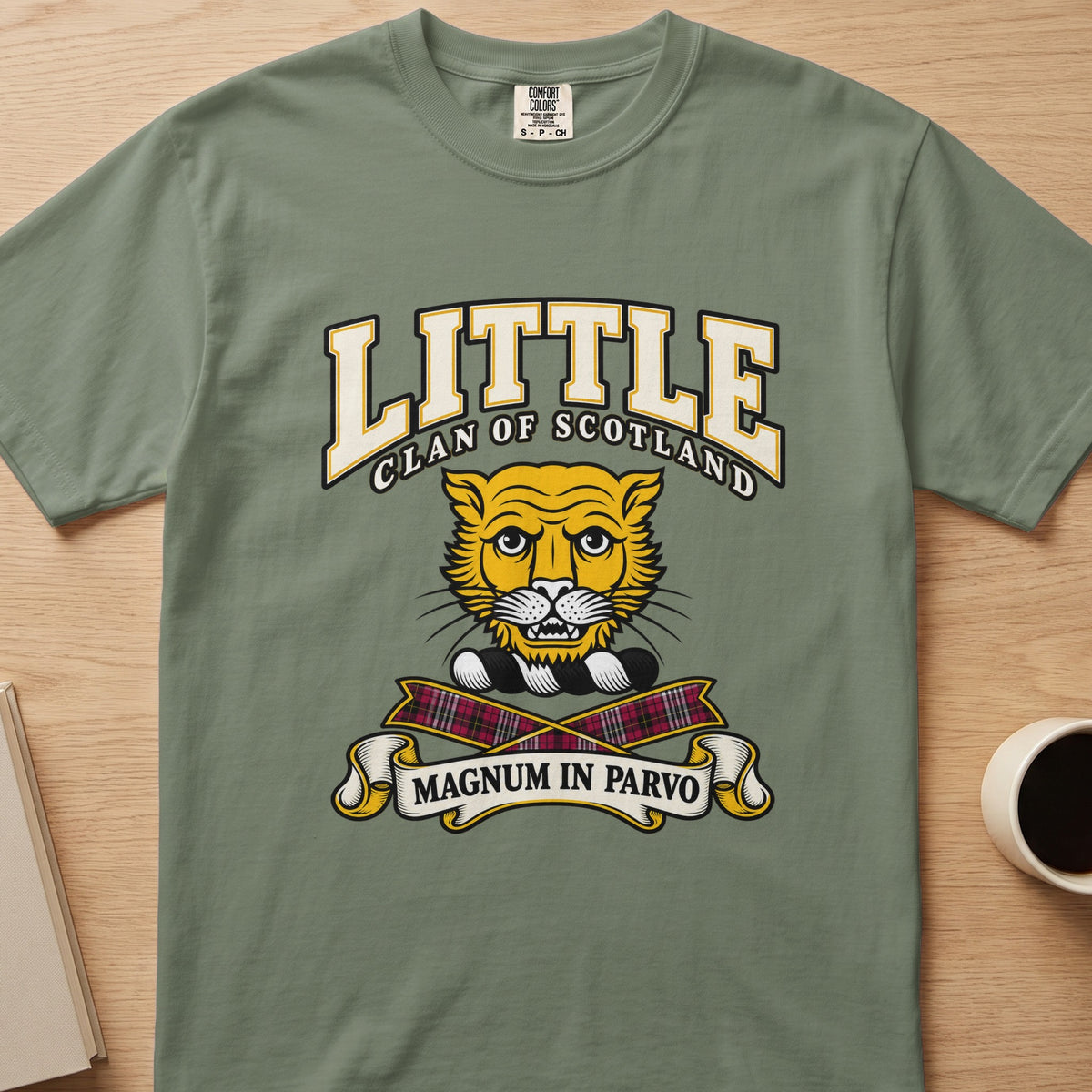 Little clan crest with gold cat face on a sage green Comfort Colors T-shirt, front view