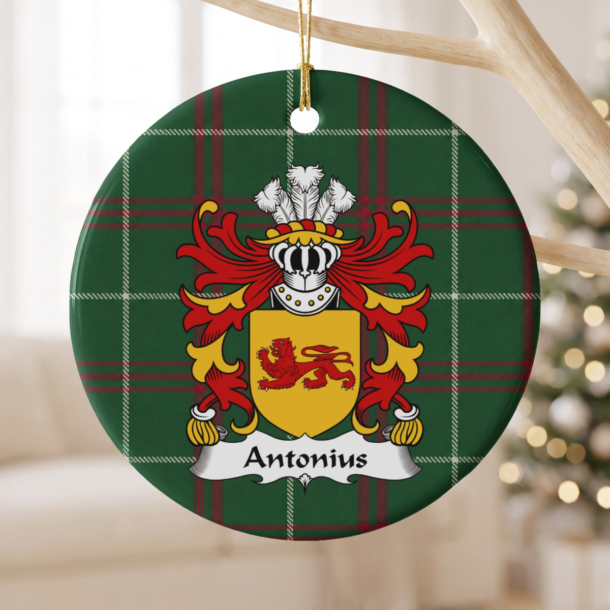 Antonius family crest and surname on a round Welsh national tartan ornament, hanging by a gold cord from a pale wooden branch with blurred Christmas lights behind it.
