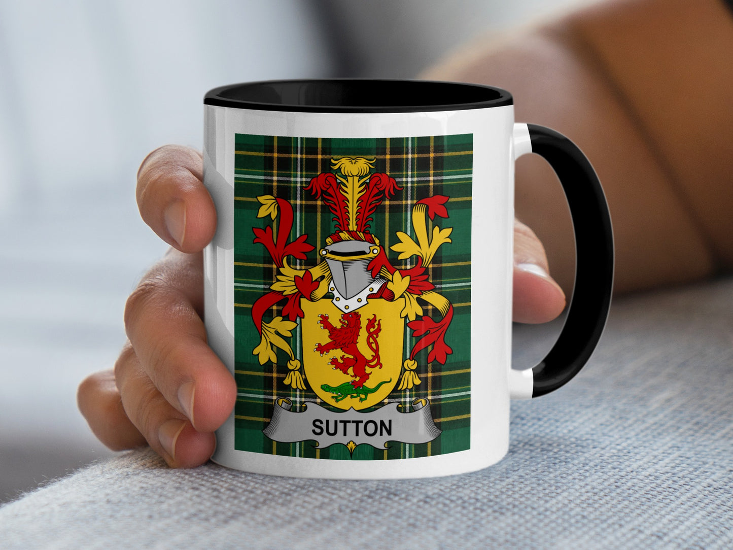 White mug with black handle featuring the Sutton family crest on a green tartan background.