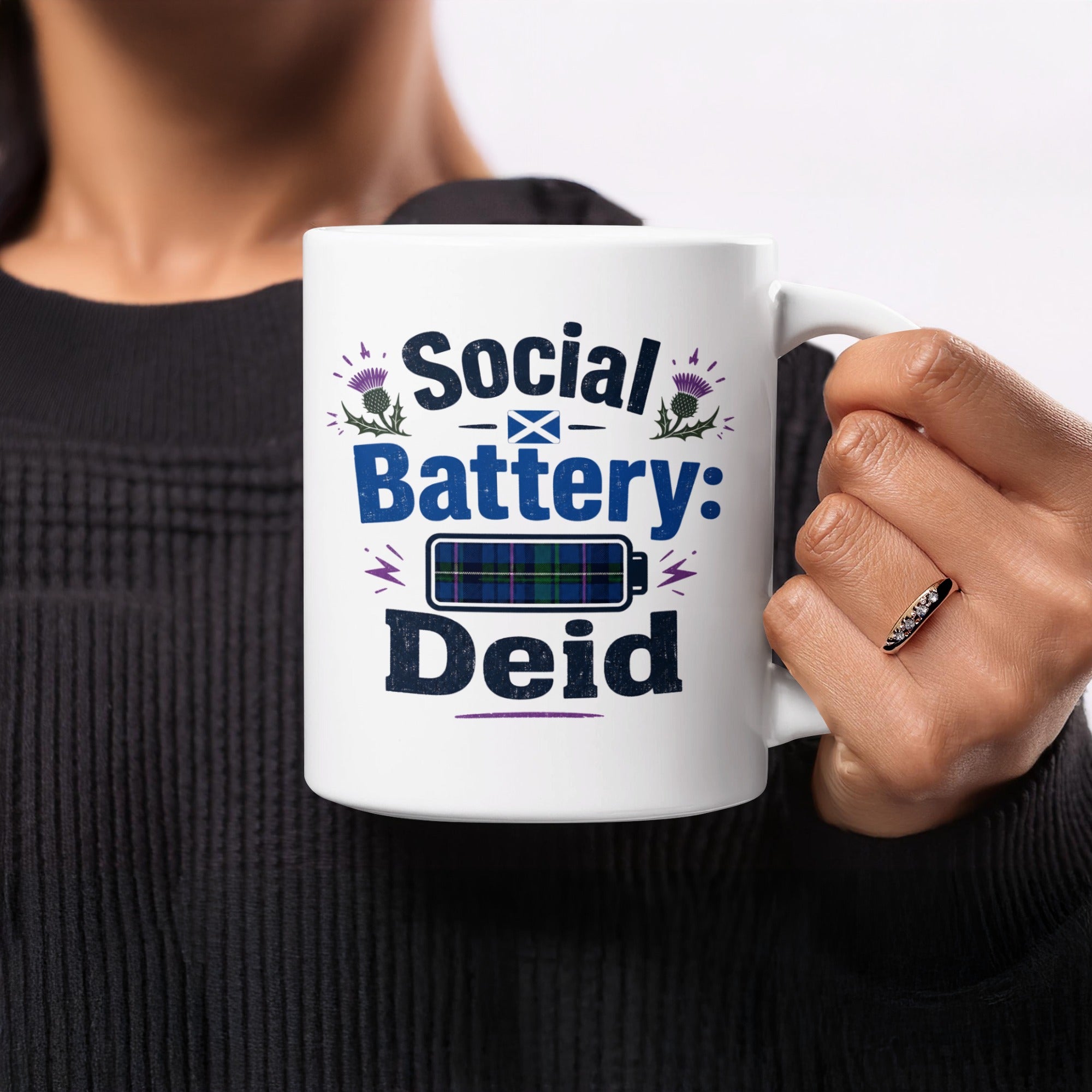 White mug with "Social Battery: Deid" and Scottish thistle graphics.
