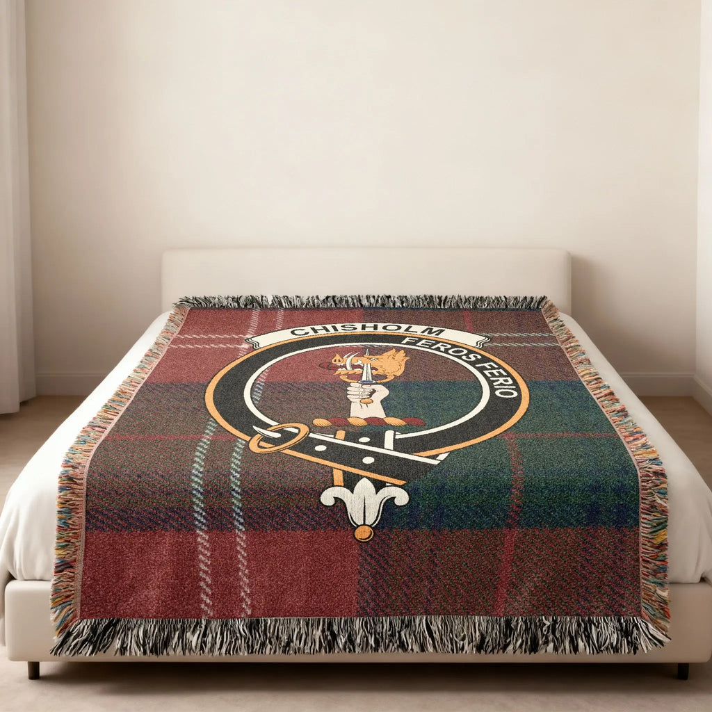 Chisholm clan tartan woven blanket in room setting — crest at centre, fringe edge visible