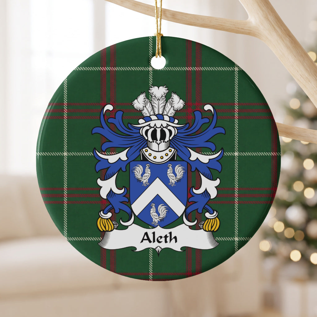 Aleth family crest and surname on a round Welsh national tartan ornament, hanging by a gold cord from a pale wooden branch with blurred Christmas lights behind it.