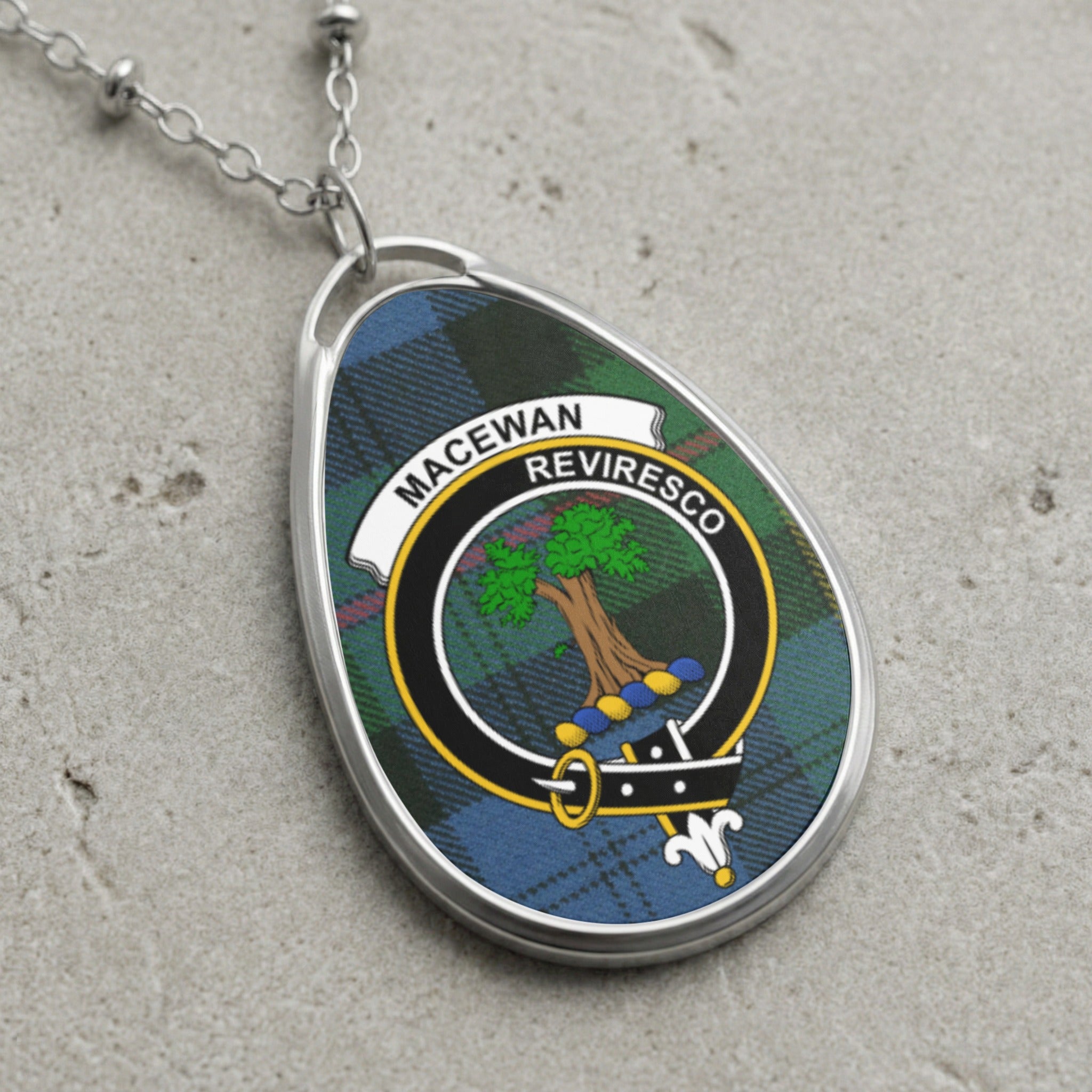 Oval pendant with MacEwan Reviresco crest on tartan, hanging from silver chain.