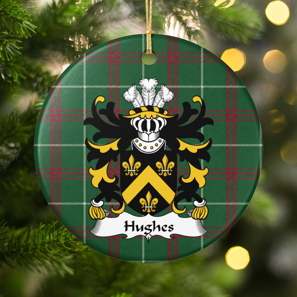 Hughes Style 1 ornament hanging among Christmas tree branches and warm lights; a gold chevron and three gold fleurs-de-lis on a black shield on Welsh national tartan.
