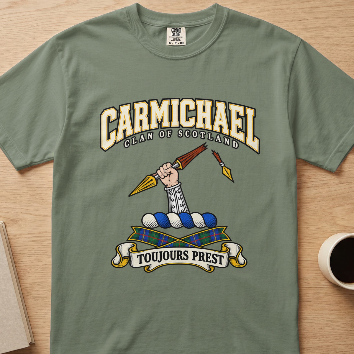Carmichael clan crest with armored arm and broken spear on a sage green Comfort Colors T-shirt, front view