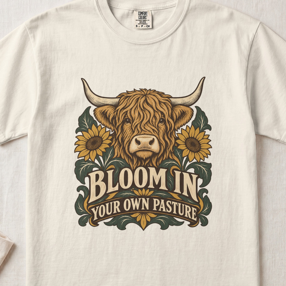 Bloom in Your Own Pasture Highland cow design on an Ivory Comfort Colors 1717 T-shirt, flat lay