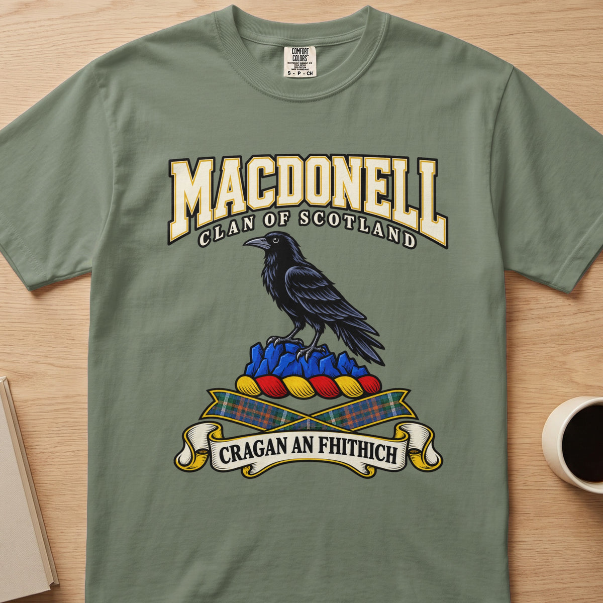 MacDonell dark bird perched on blue rocks graphic on a sage green Comfort Colors T-shirt, front view