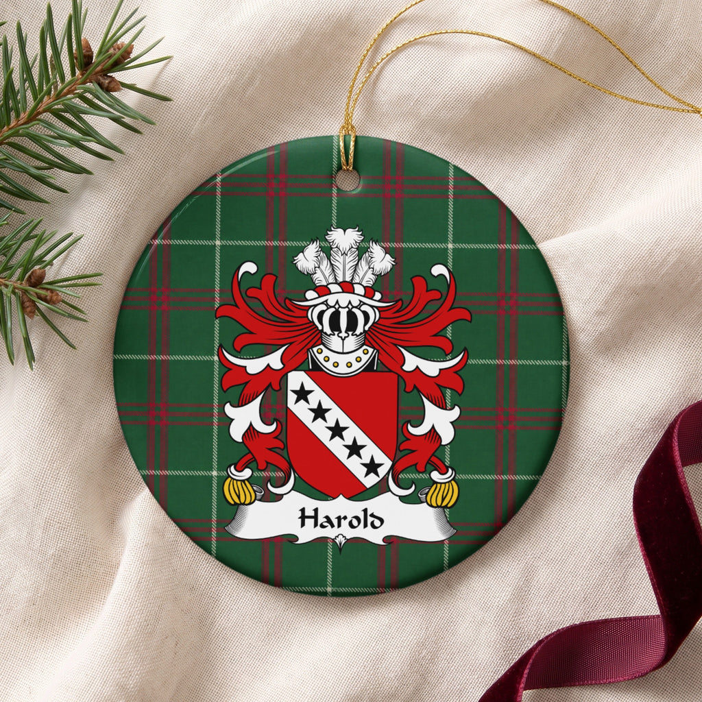 Harold ornament on cream fabric beside evergreen and burgundy ribbon, with gold string; five black stars on a white diagonal band across a red shield.