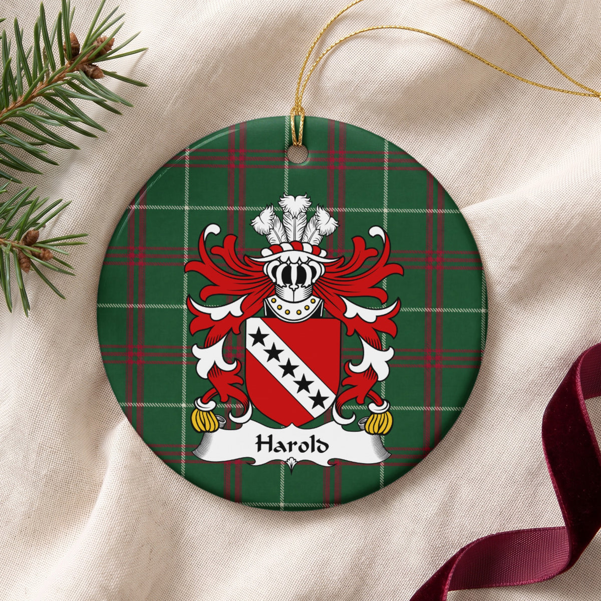 Harold ornament on cream fabric beside evergreen and burgundy ribbon, with gold string; five black stars on a white diagonal band across a red shield.