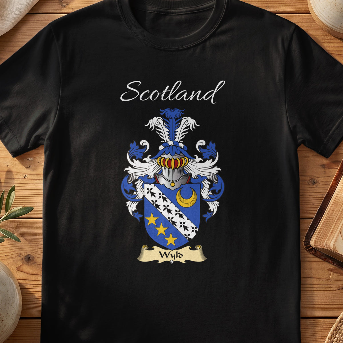 Black Wyld Scottish family crest T-shirt laid flat, showing “Scotland” above a blue-and-gold shield crossed by a diagonal band of stars.