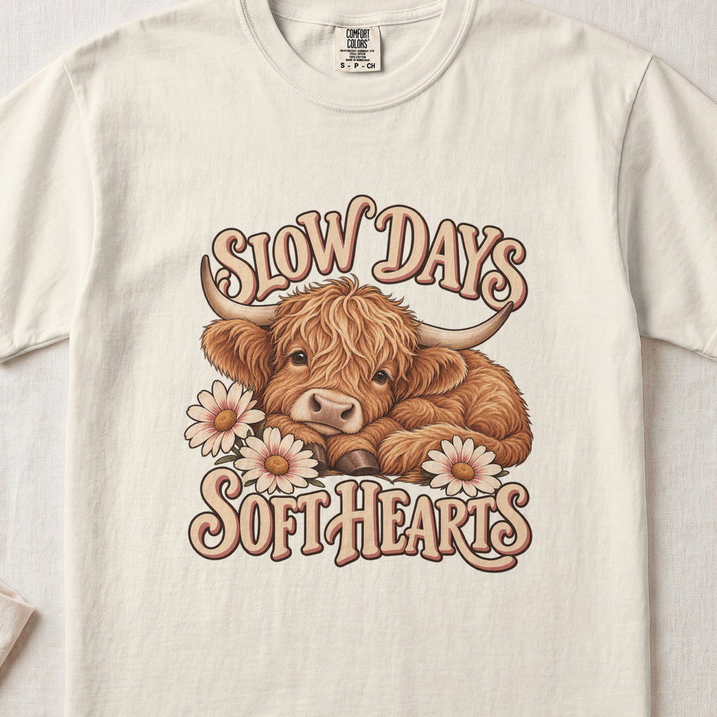 Slow Days, Soft Hearts Highland cow design on an Ivory Comfort Colors 1717 T-shirt, flat lay