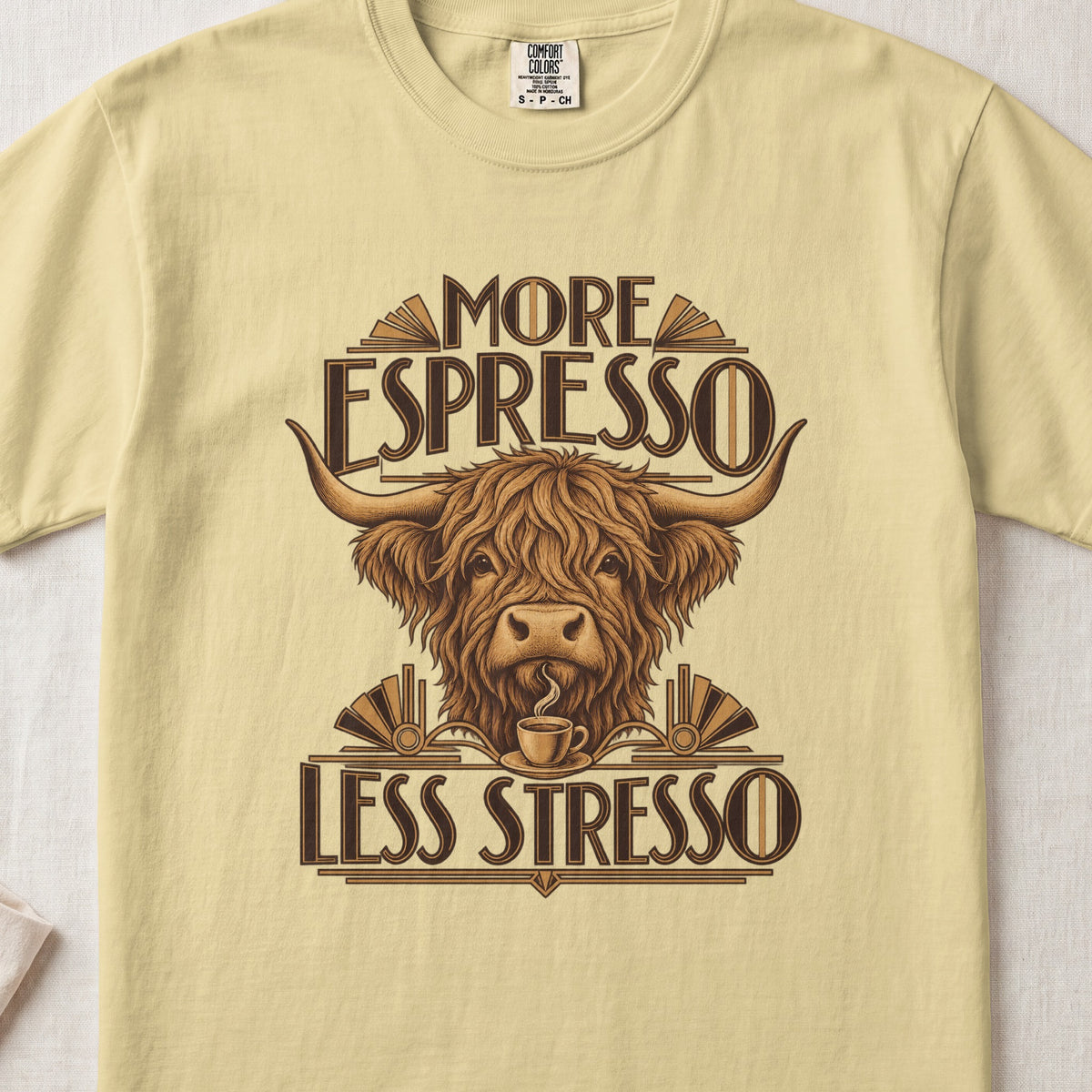 More Espresso, Less Stresso Highland cow design on a Butter Comfort Colors 1717 T-shirt, flat lay