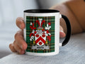 White family crest on a black and white mug held by a hand.