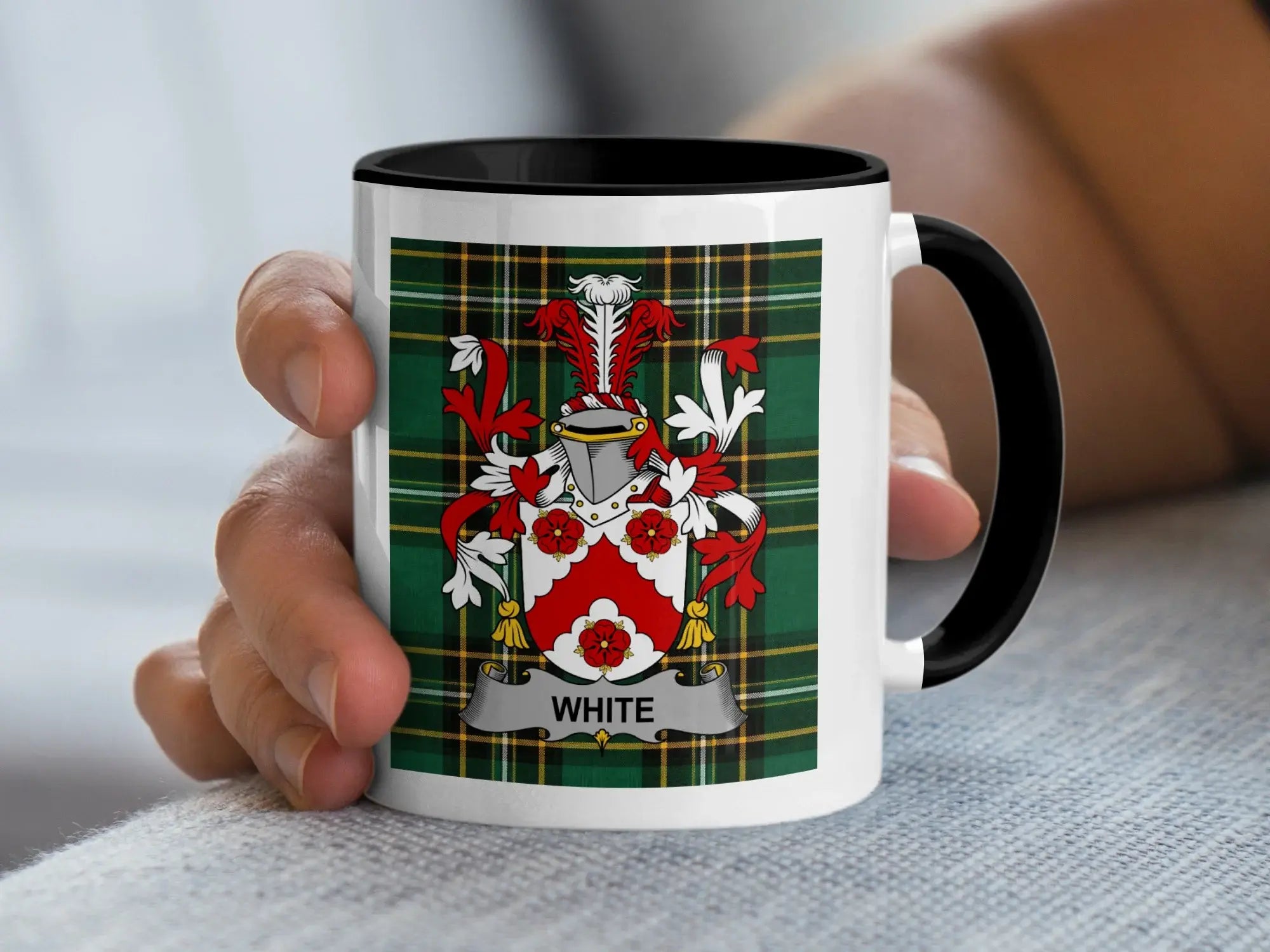 White family crest on a black and white mug held by a hand.