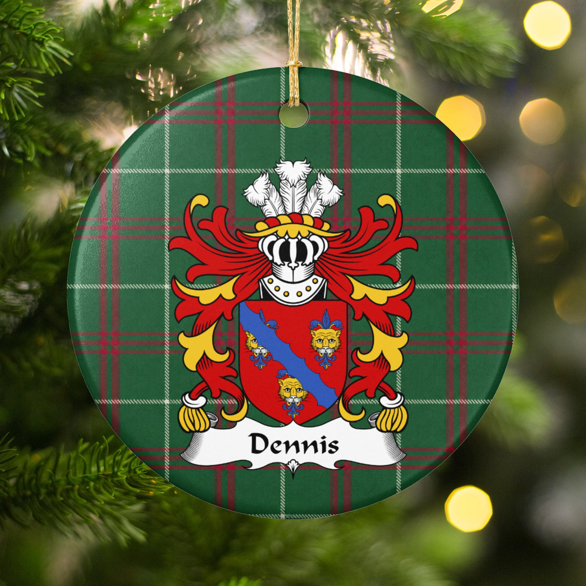 Dennis ornament hanging among Christmas tree branches and warm lights; three gold faces and a blue diagonal band on a red shield on Welsh national tartan.
