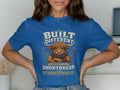 Blue t-shirt with highland cow graphic and text "Built Different Mostly Shortbread and Stubbornness".